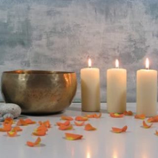 Bild von einer Klangschale 3 weissen Kerzen und Blütenblättern